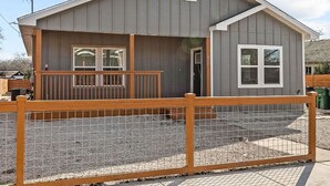 A two-story building with a grey exterior, a wooden deck, and a fenced front yard. - Retreat to a Brand-new Downtown Home 4BR 3BA (San Antonio)