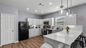 A modern kitchen with white cabinetry, a black refrigerator, stainless steel appliances, and a central island with bar stools. - Retreat to a Brand-new Downtown Home 4BR 3BA (San Antonio)