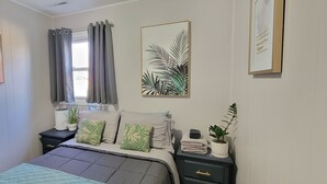 Un dormitorio con cama, mesitas de noche, una ventana con cortinas y decoración en la pared.