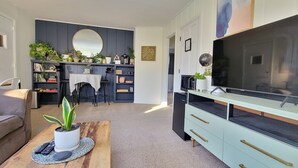 Una sala moderna con un televisor de pantalla plana grande, una mesa de centro con una planta, un sofá y un comedor con sillas y una mesa.