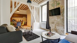 A modern living room with a sofa, a coffee table, and a TV mounted on the wall. There is a kitchen visible in the background. - 377 Suite Stella - Superb apartment in Paris (Paris 03 Temple)
