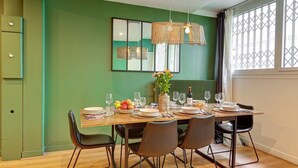 Ein Essbereich mit grüner Wand, einem Holztisch für sechs Personen und einer hängenden Leuchte.