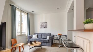Ein modernes Wohnzimmer mit einem grauen Sofa, einem Holzstuhl, einem kleinen runden Tisch mit einer Flasche und Gläsern sowie einer Heizung.