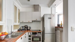 Eine kompakte Küche mit weißen Schränken, einem Edelstahlkühlschrank, einer Kaffeemaschine und einem eingebauten Backofen.