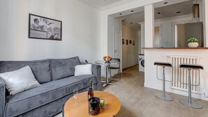 Ein modernes Wohnzimmer mit einem grauen Sofa, einem Couchtisch mit Flasche und Glas sowie einem Essbereich mit einer Fruchtschale.