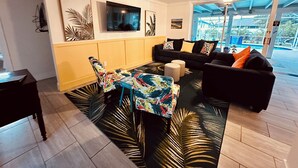 Ein modernes Wohnzimmer mit Sofa, Fernseher und Blick auf einen Außenpool.