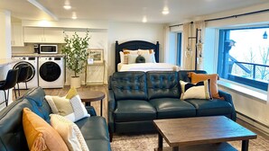 A modern hotel room with a bed, a sofa, a coffee table, a dining table, a kitchen area with a washing machine, and a view of the outside. - Location and panoramic lake views will make for an unforgettable experience.  (Duluth)
