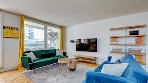A modern living room with a green sofa, a blue sofa, a TV, and a bookshelf. - 825 Suite Bacla - Superb apartment (Courbevoie)