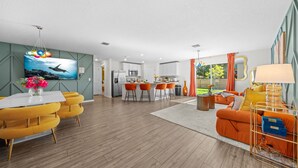 Ein modernes Wohnzimmer mit Essbereich, Küche und einem großen Fernseher.