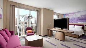 A hotel room with a large bed, a sofa, a TV, and a desk.