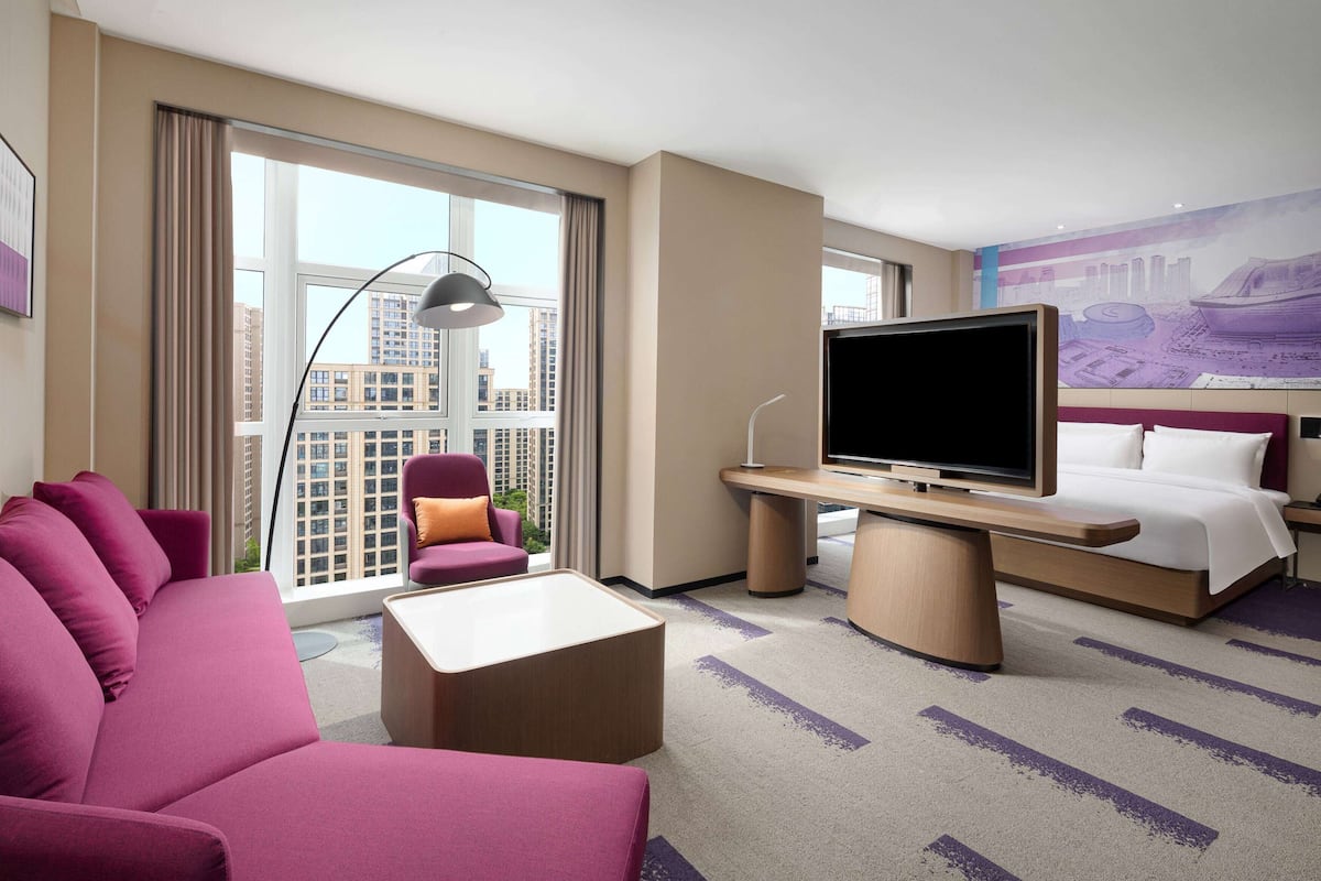 A hotel room with a large bed, a sofa, a TV, and a desk.