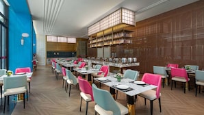 A modern dining area with multiple tables and chairs, a kitchen area with shelves, and a blue accent wall. - Ramada By Wyndham Yichang Riverside (Yichang)