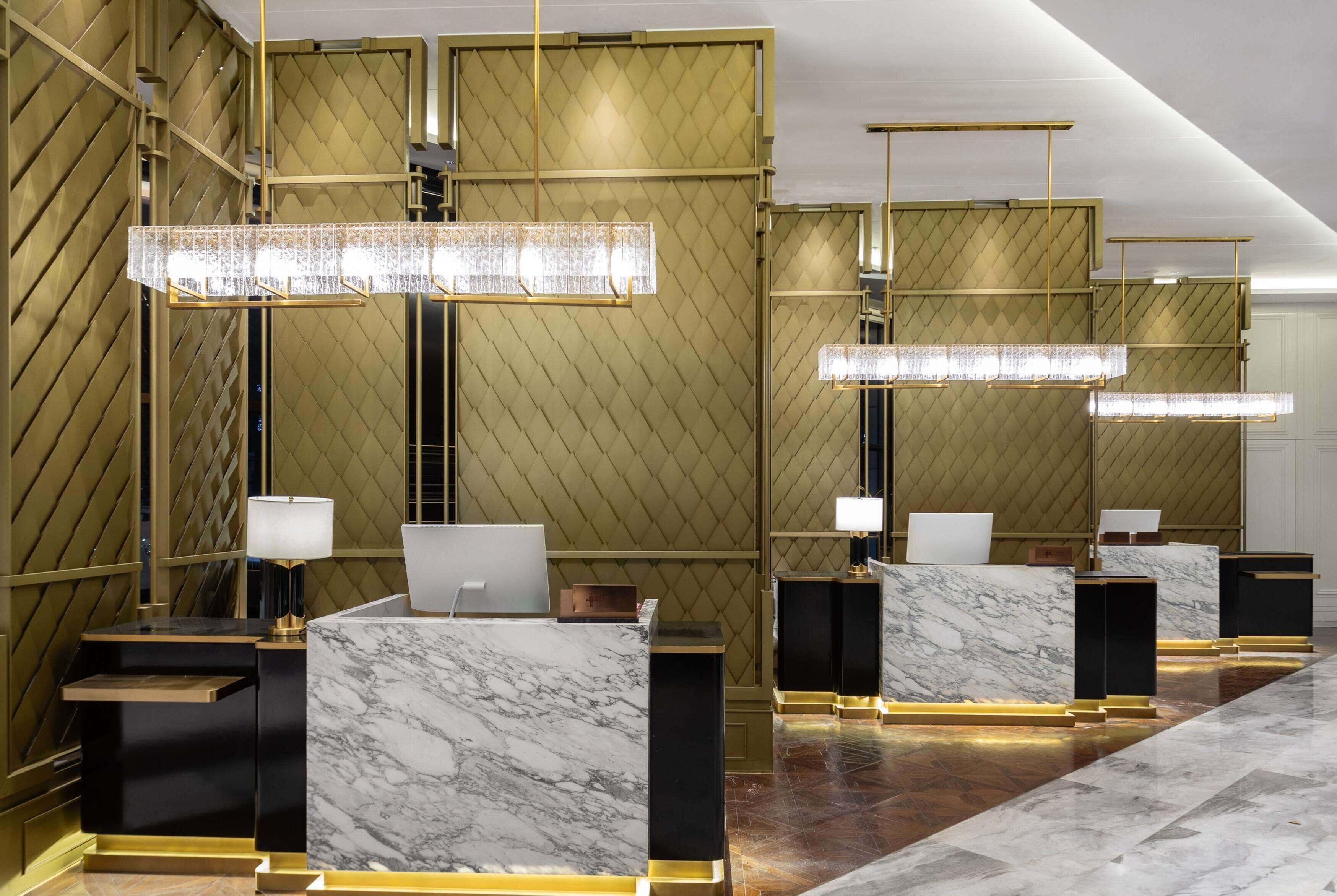 A reception area with marble counters, gold accents, and pendant lighting.