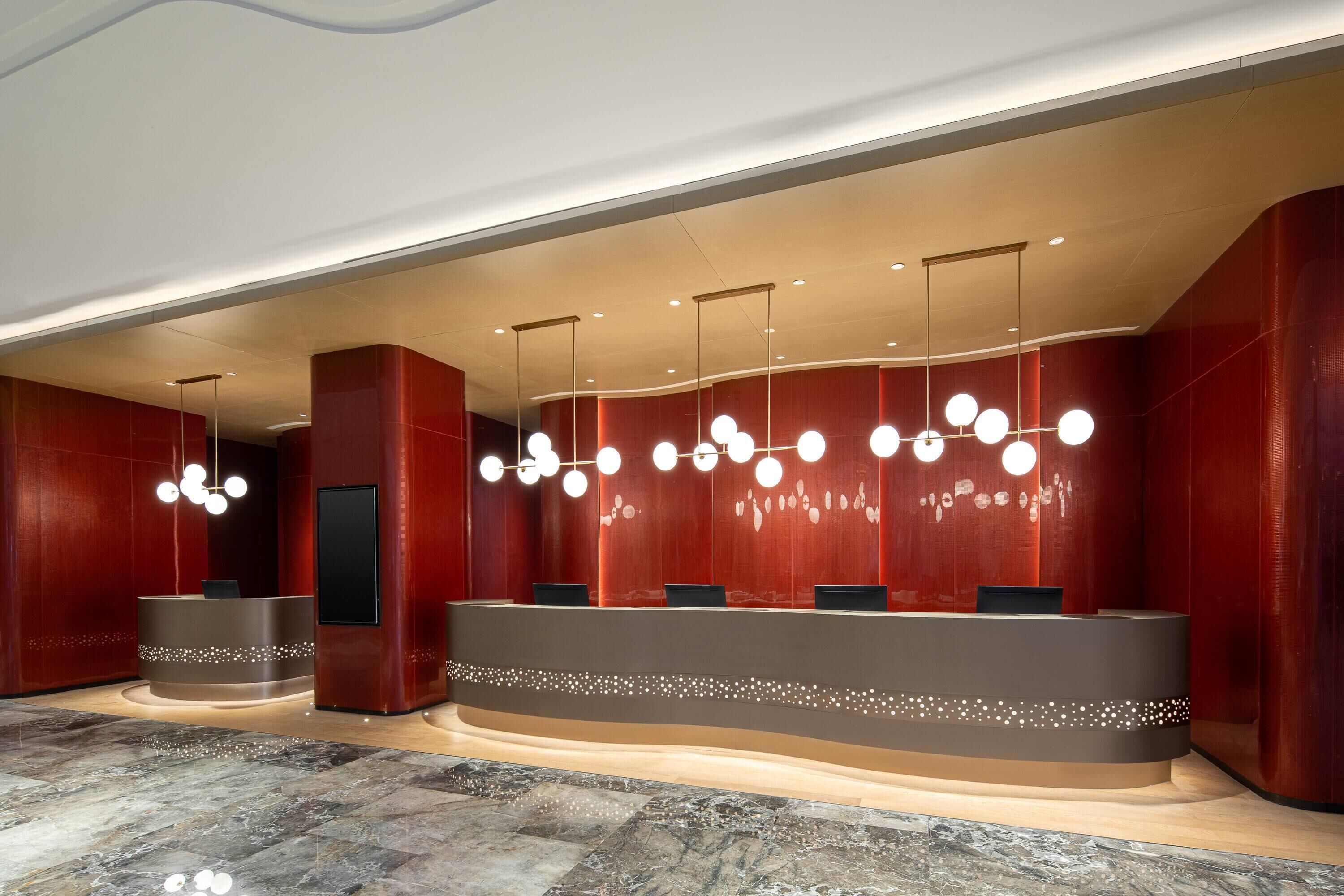 Un área de recepción moderna con un mostrador curvo, varias luminarias y suelo de mármol.