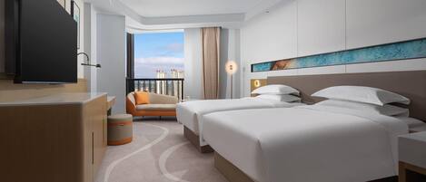 A modern hotel room with two beds, a desk, a TV, and a balcony with a city view.