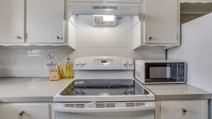 Une cuisine avec des meubles blancs, une cuisinière, un four à micro-ondes et un bloc à couteaux.