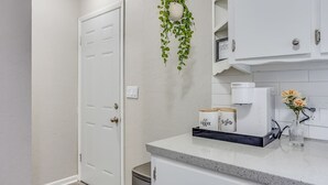 Une cuisine moderne avec des meubles blancs, un plan de travail, une machine à café et une plante suspendue.