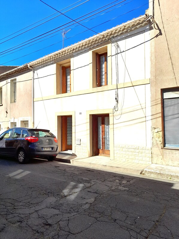 Un bâtiment à deux étages, doté d’un toit recouvert de tuiles, une voiture Citroën garée devant, et des câbles électriques apparents.