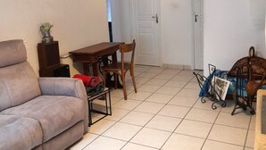 A living room with a sofa, a wooden table, and a chair. There is a door in the background leading to another room. - L'ase et la Tuca (Bessan)