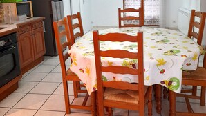 A dining area with a round table covered by a floral tablecloth, surrounded by wooden chairs. - L'ase et la Tuca (Bessan)