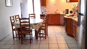 A kitchen with wooden cabinets, a tiled floor, a dining table with chairs, and a refrigerator. - L'ase et la Tuca (Bessan)