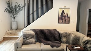 En stue med sofa, en potteplante, et maleri og en trappe.