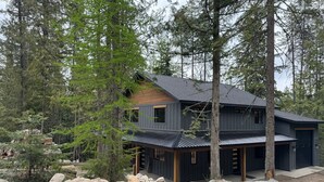 Et moderne hus med to etager, mørkt ydre og tæt skov samt store sten omkring.