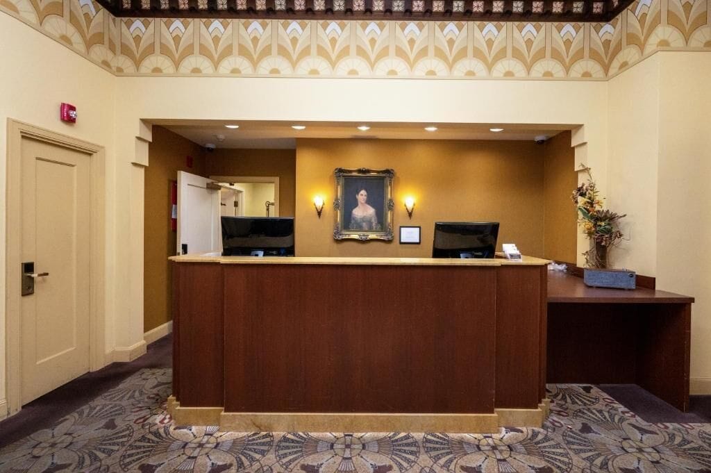 A reception desk with a framed portrait, two wall-mounted lights, and a potted plant.