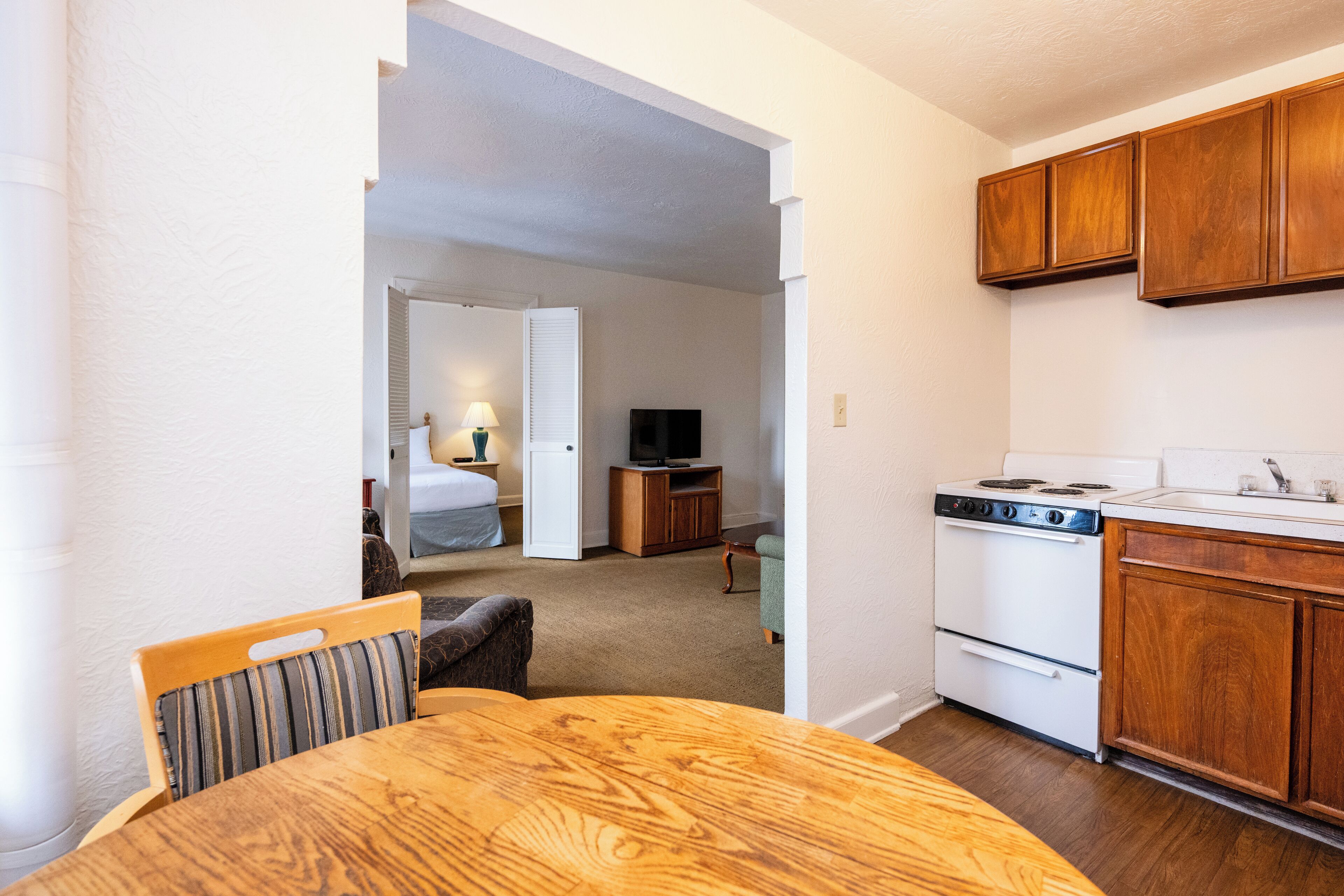A compact kitchen with wooden cabinets, a stove, and a dining area with a table and chairs.