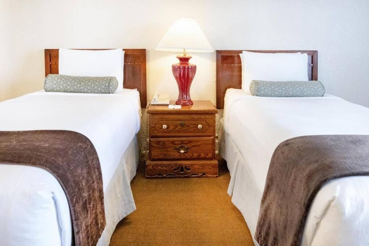 A hotel room with two single beds, a wooden nightstand with a lamp, and a small wooden chest of drawers.