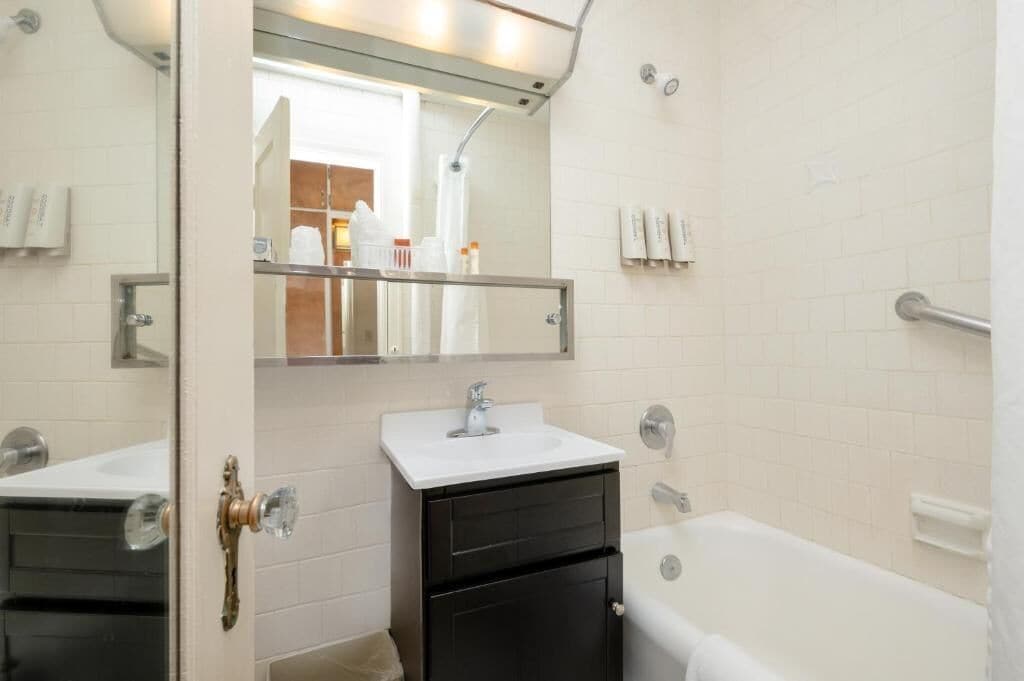 A bathroom with a white sink, a mirror, a black cabinet, and a white bathtub.