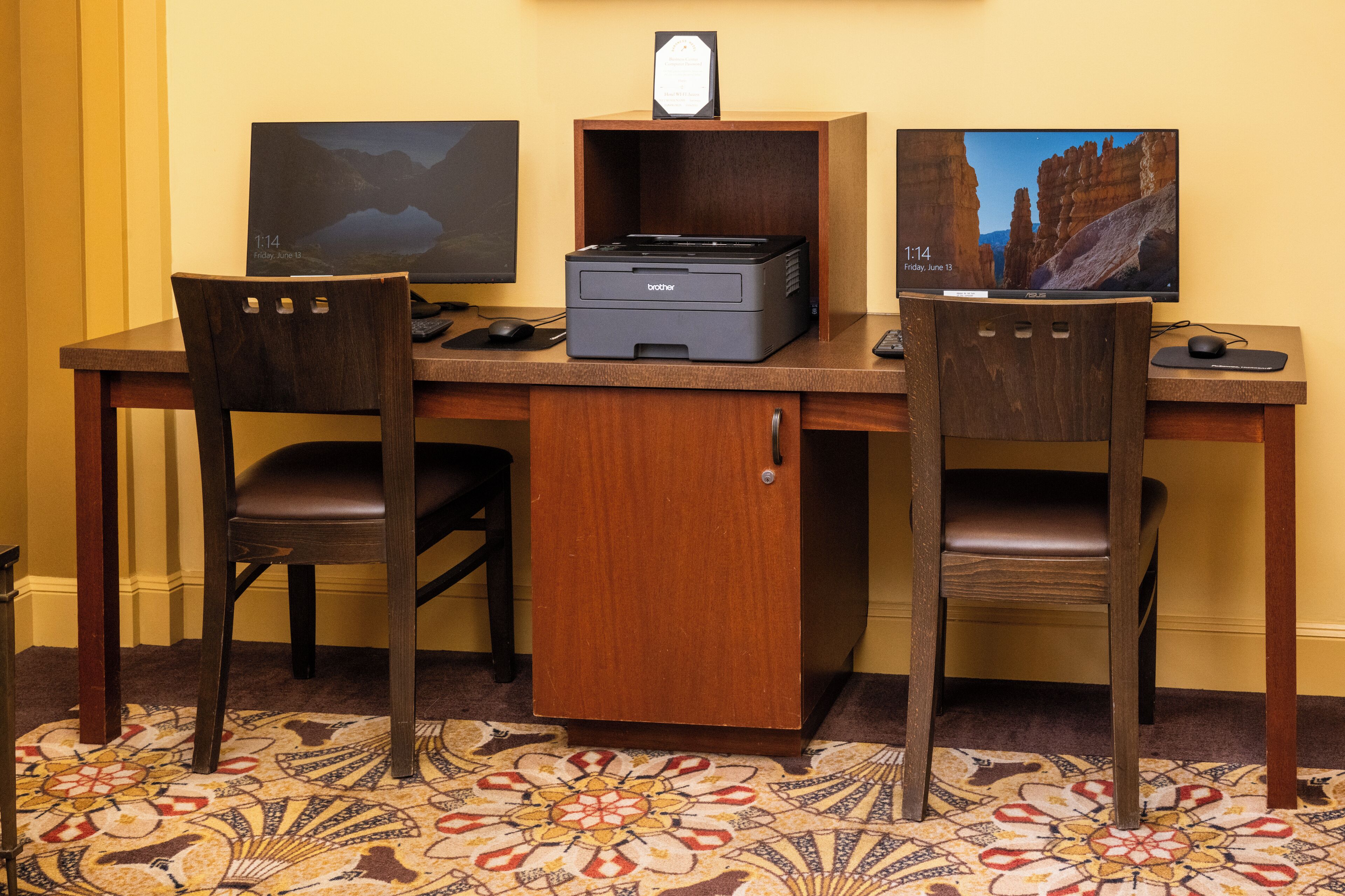 A wooden desk with two monitors, a printer, and two chairs.