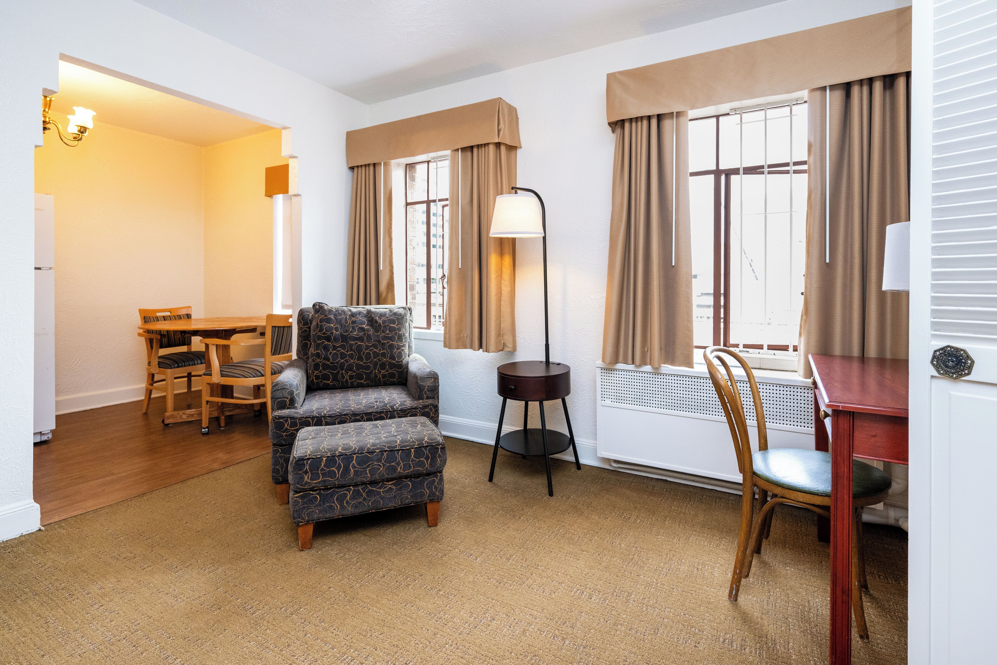 A hotel room with a dining area, a sofa, a lamp, and a chair.