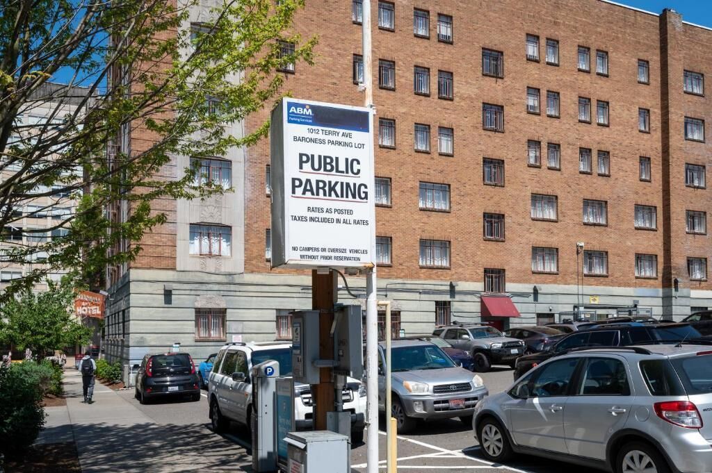 A public parking sign in front of a brick building with multiple windows.