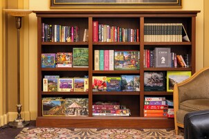A bookshelf filled with books and puzzles, a patterned carpet, and a lamp.
