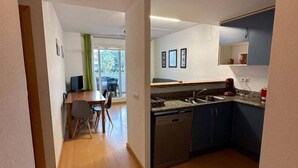 A compact kitchen with a dishwasher, a sink, and a countertop. There is a dining area with a table and chairs, and a view of the outdoors through a window. - Apartment with communal swimming pool AV 29 (Rosas / Roses)