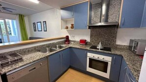 A compact kitchen with blue cabinets, a granite countertop, a built-in oven, and a dishwasher. - Apartment with communal swimming pool AV 29 (Rosas / Roses)