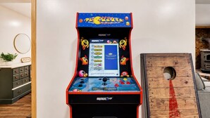 Une borne d’arcade Pac-Man dans une pièce avec un meuble en bois et un miroir rond accroché au mur.