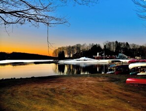 A lakeside view with a row of canoes and a building in the background. - House in the Trees Ski, Swim in The Hideout (Lake Ariel)