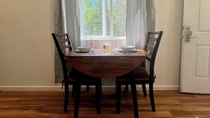 Een eetgedeelte met een houten tafel en stoelen, een raam met gordijnen en een deur.