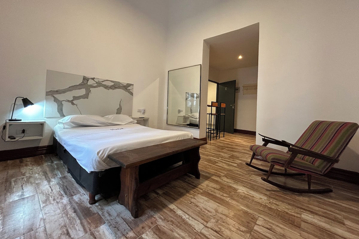 A bedroom with a bed, a nightstand, a lamp, a chair, and a mirror.