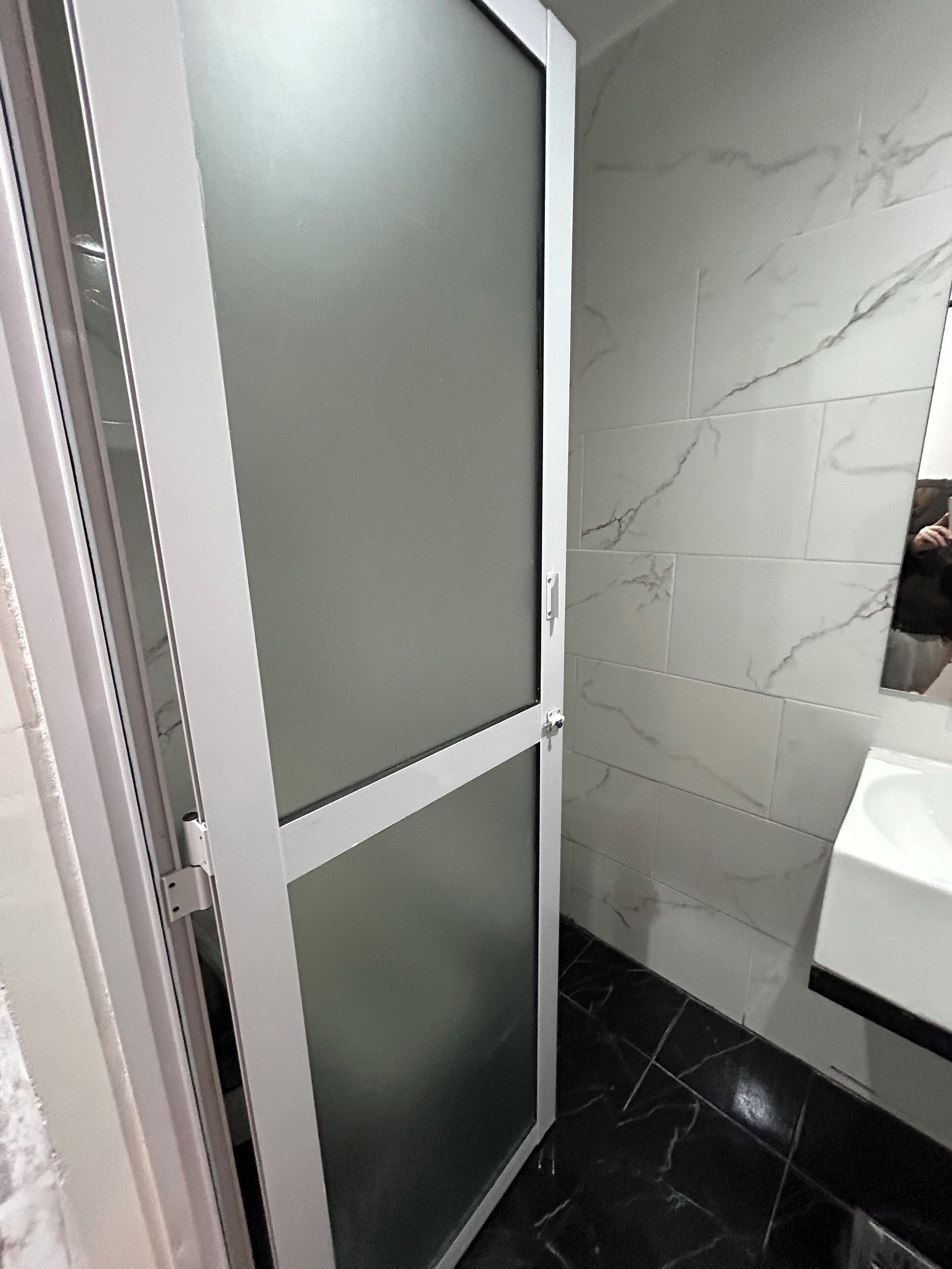 Une salle de bain avec un lavabo blanc, un miroir et une douche dotée d’une porte en verre.