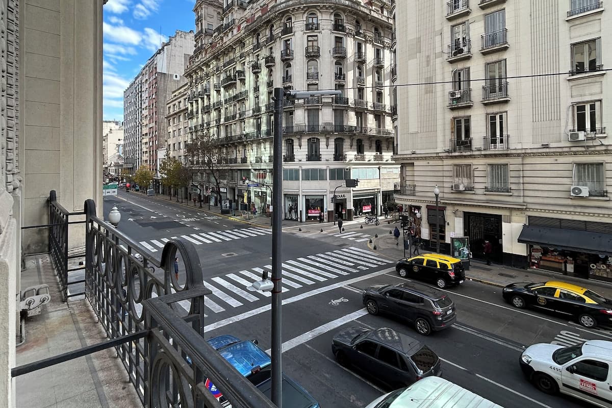 A city street with a large, ornate building in the background, a crosswalk, and various vehicles including a white van and a yellow taxi.