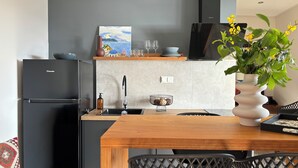 A modern kitchen with a black refrigerator, a wooden dining table, and a black chair. - CACTUS SUPERB SUITE WITH PRIVATE POOL AND STUNNING SEA VIEWS (SKIATHOS)