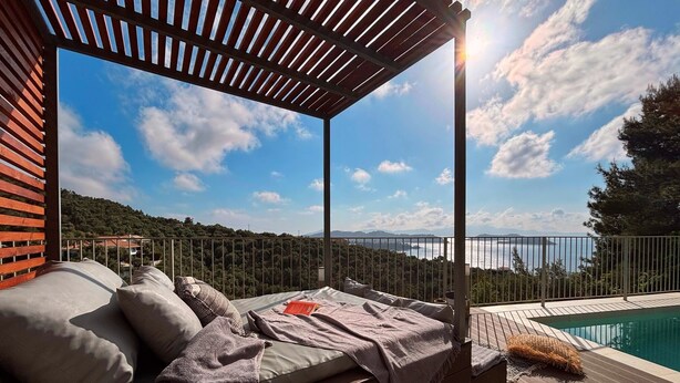 A sunlit outdoor seating area with a view of a body of water and hills. - CACTUS SUPERB SUITE WITH PRIVATE POOL AND STUNNING SEA VIEWS (SKIATHOS)