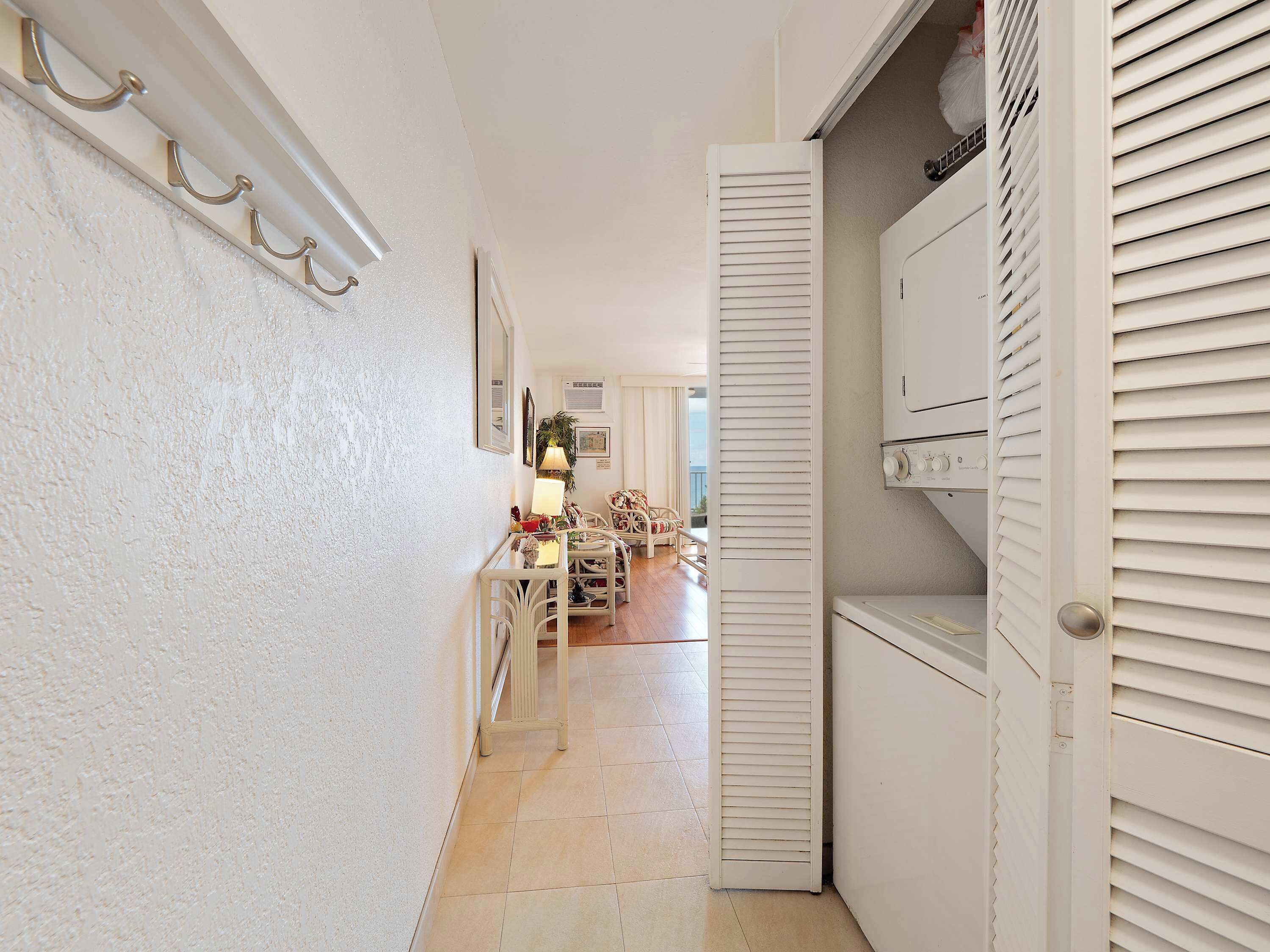A hallway with a white wall, a door with louvered shutters, and a glimpse of a dining area with chairs and a table.