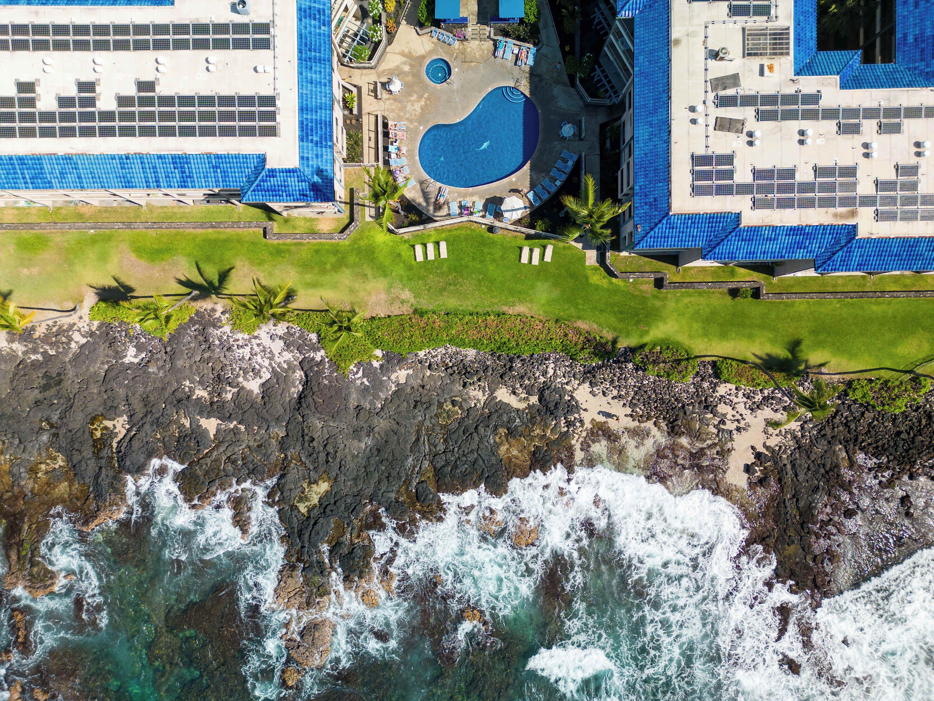 Vista aérea de un complejo turístico con piscina, sillas de descanso y una costa rocosa.