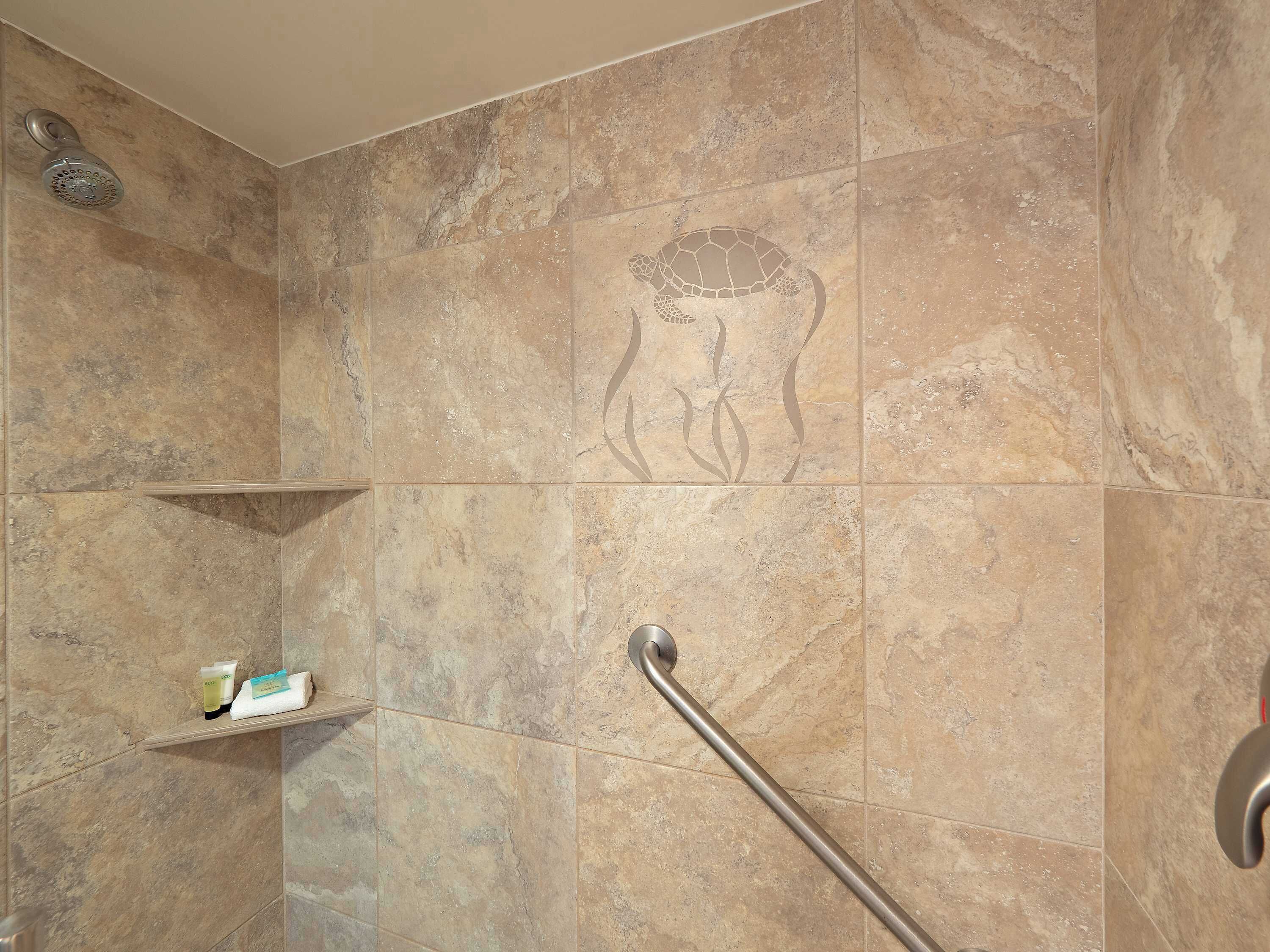Ein Duschbereich mit Haltegriff, Ablage für Toilettenartikel und einer dekorierten Fliese mit Schildkrötendesign.
