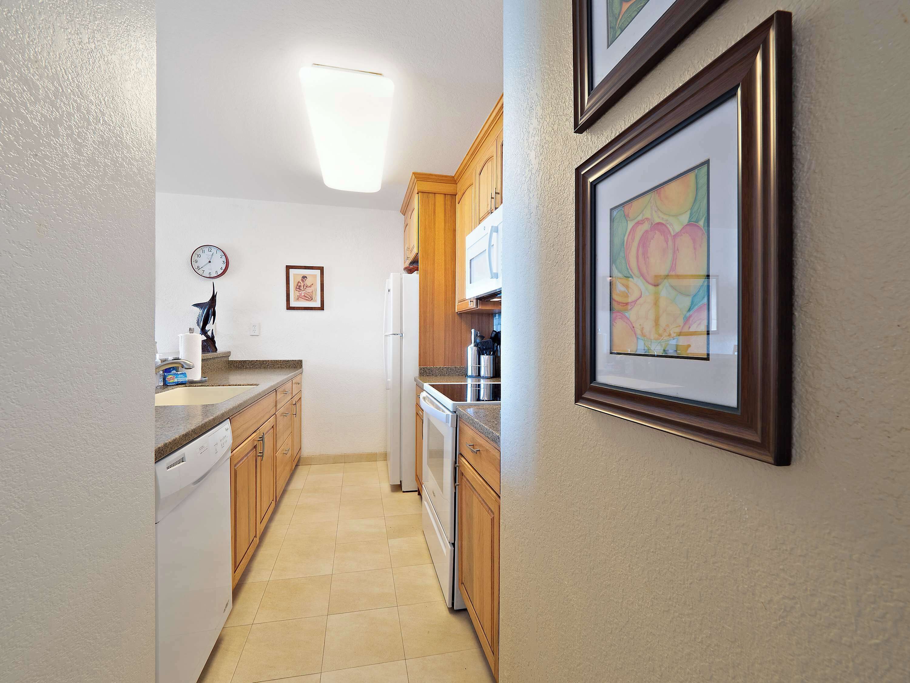 A narrow kitchen with wooden cabinets, a white refrigerator, and a clock on the wall.