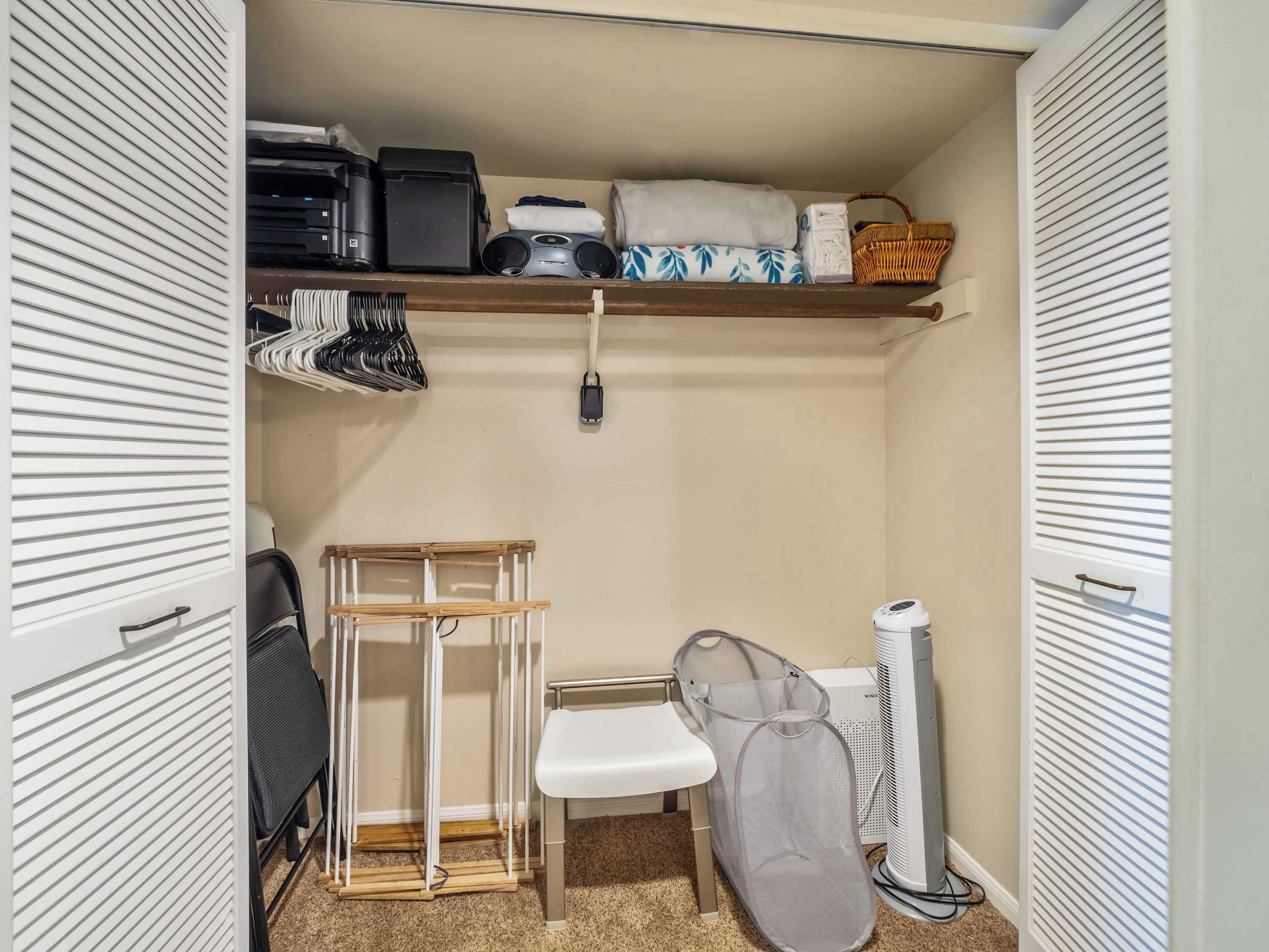 A small, organized closet with shelves, a drying rack, and a fan.